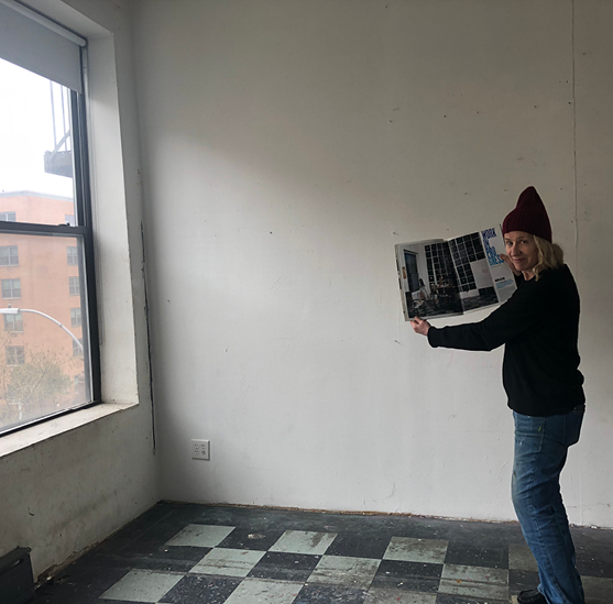 An artist holds up a magazine in her empty studio