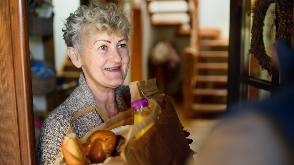 An older woman receives a bag of groceries at her door. 