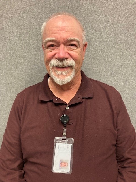 Mike, a TCOA MMAP volunteer stands smiling against a wall, wearing his tcoa badge.
