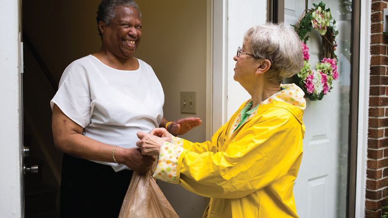 A Meals on Wheels volunteer dropping off meals to a smiling participant. 