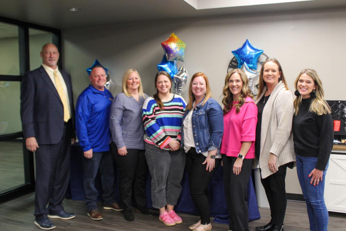 A group of people pose in a line in front of star-shaped balloons.