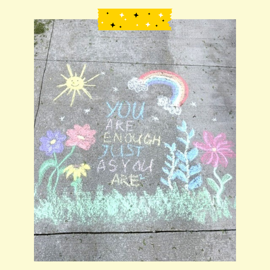 A chalk message on the ground that you are enough just as you are with flowers and grass drawn