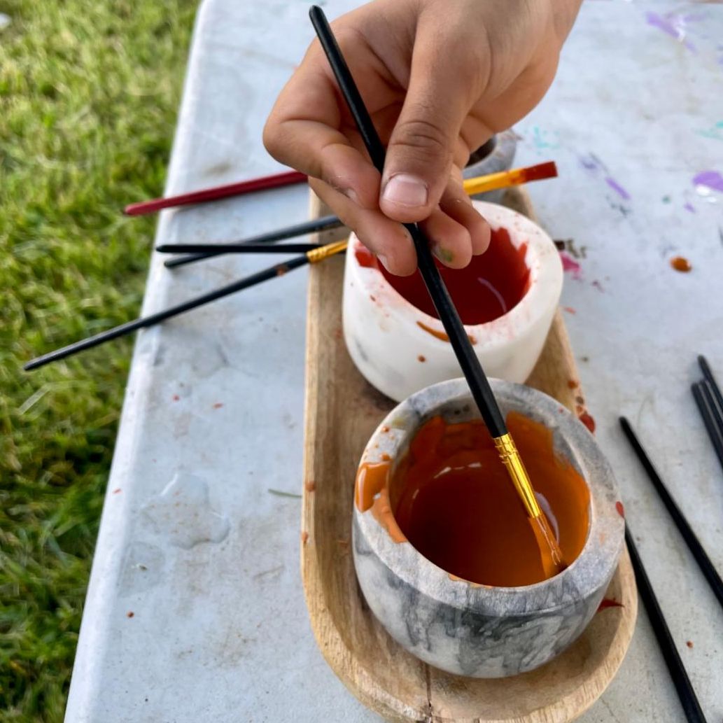 Two pots of paint on a table, hand holding a paintbrush dipping into one of the pots