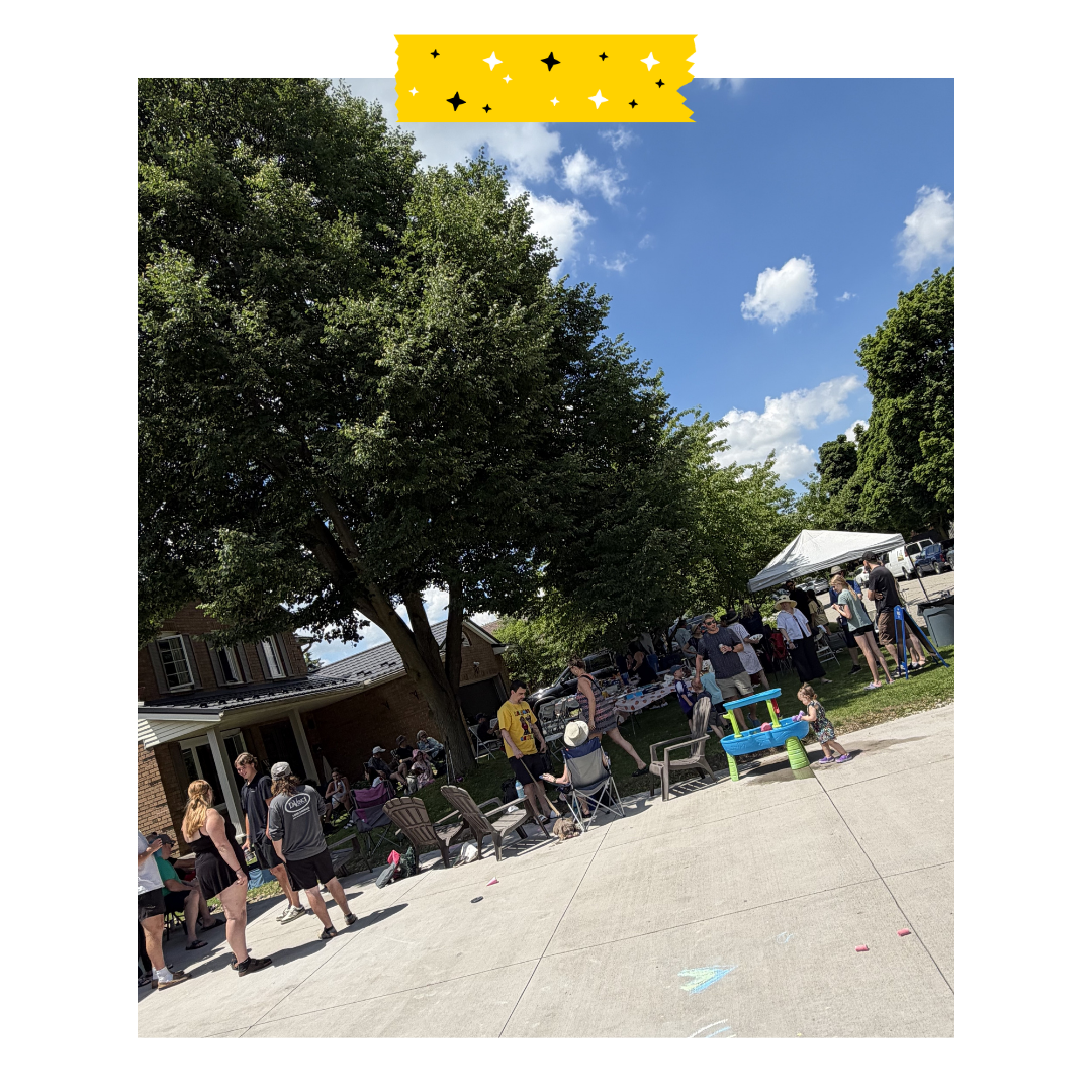 People gathered outside on a driveway and the grass enjoying food and games.