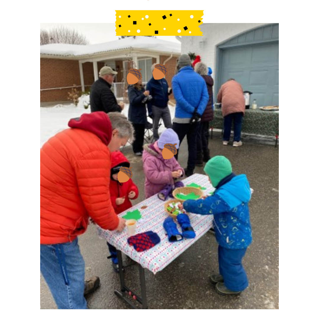 People standing outside with kids doing a craft on a table.
