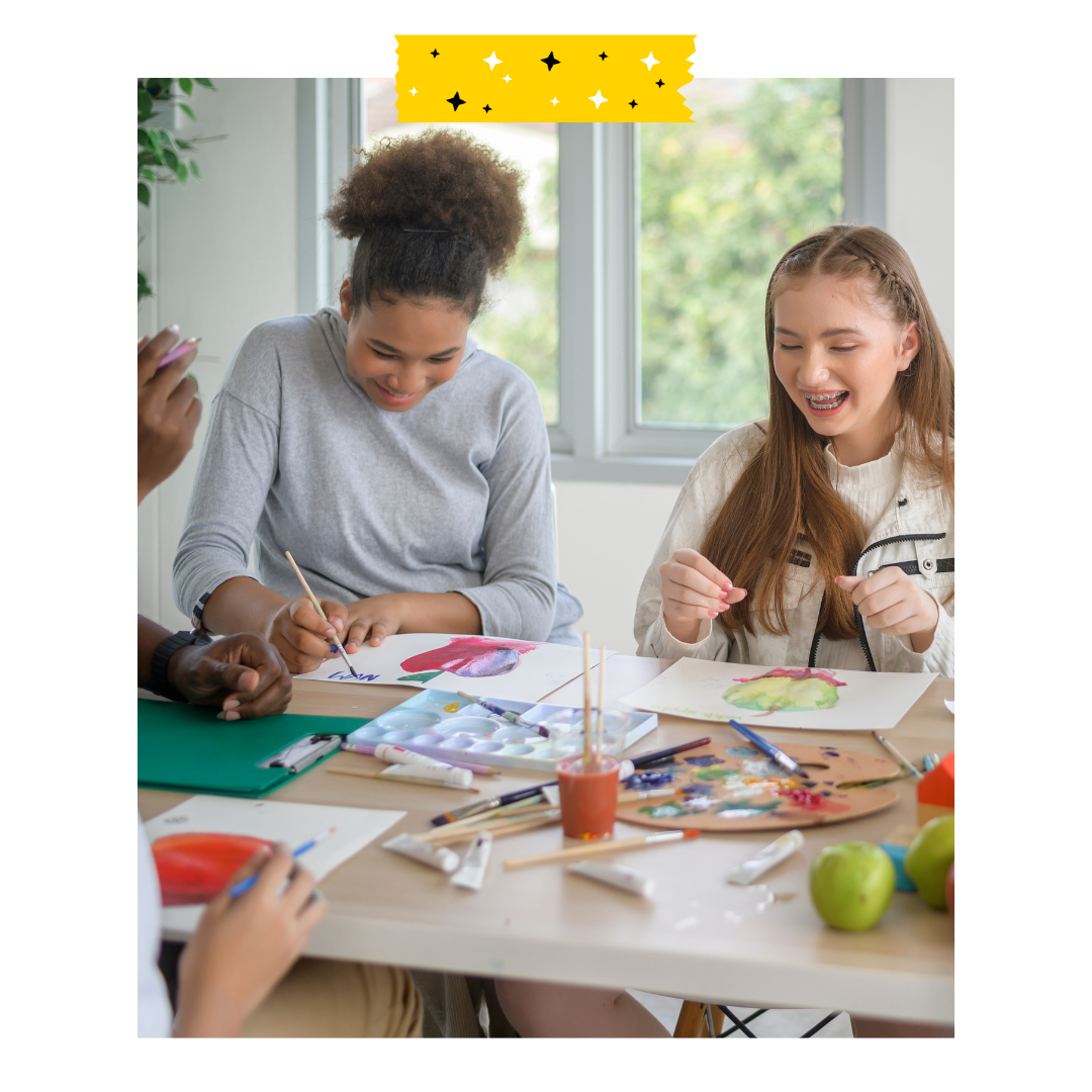 2 people sitting around a table with craft supplies in front of them.