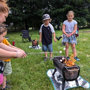 Adults and kids holding smores over an outdoor fire