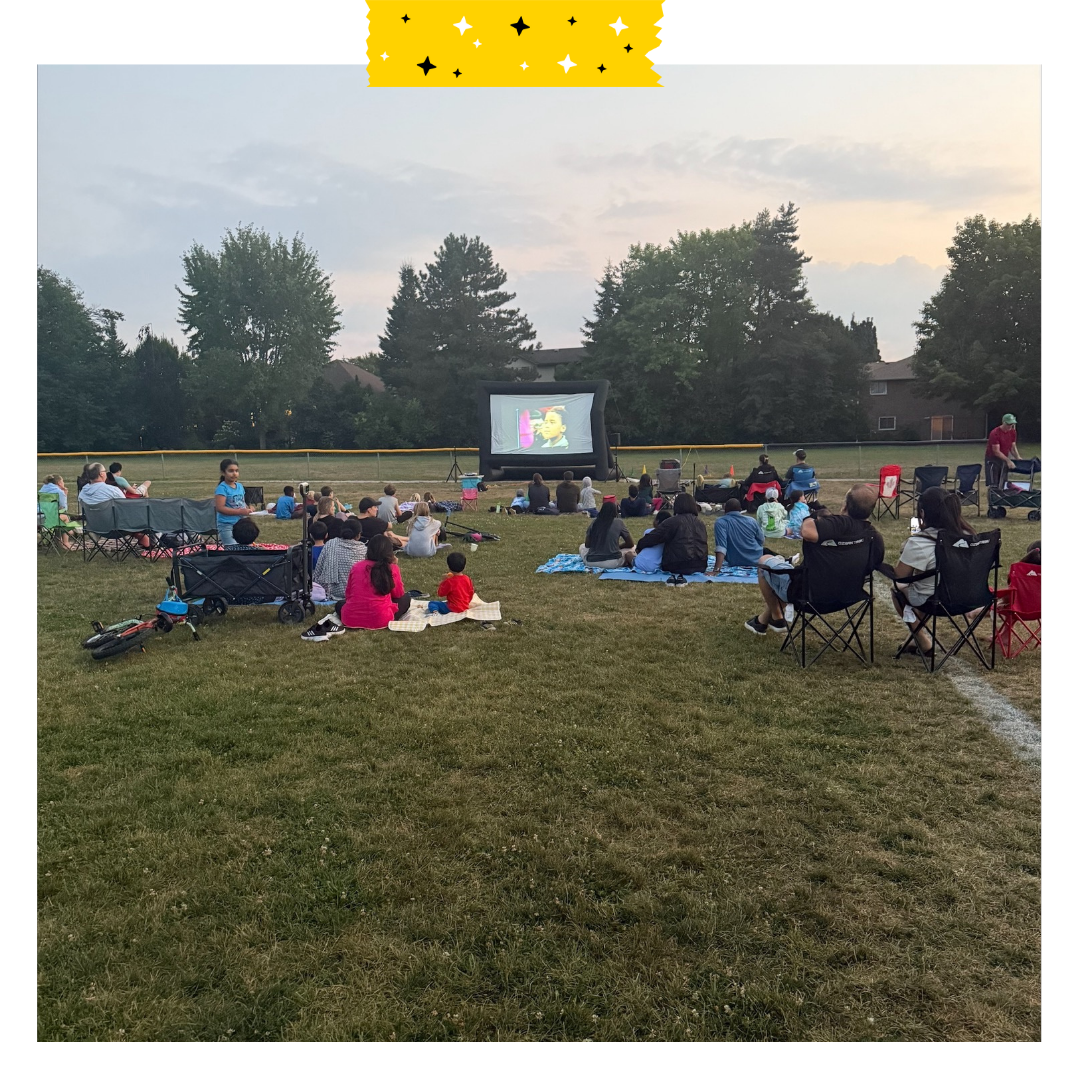 Outdoor movie set up and people sitting watching it.