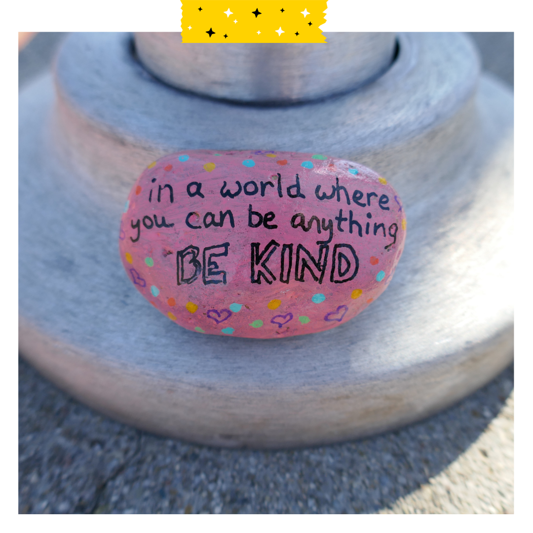 Painted rock that says in a world where you can be anything be kind
