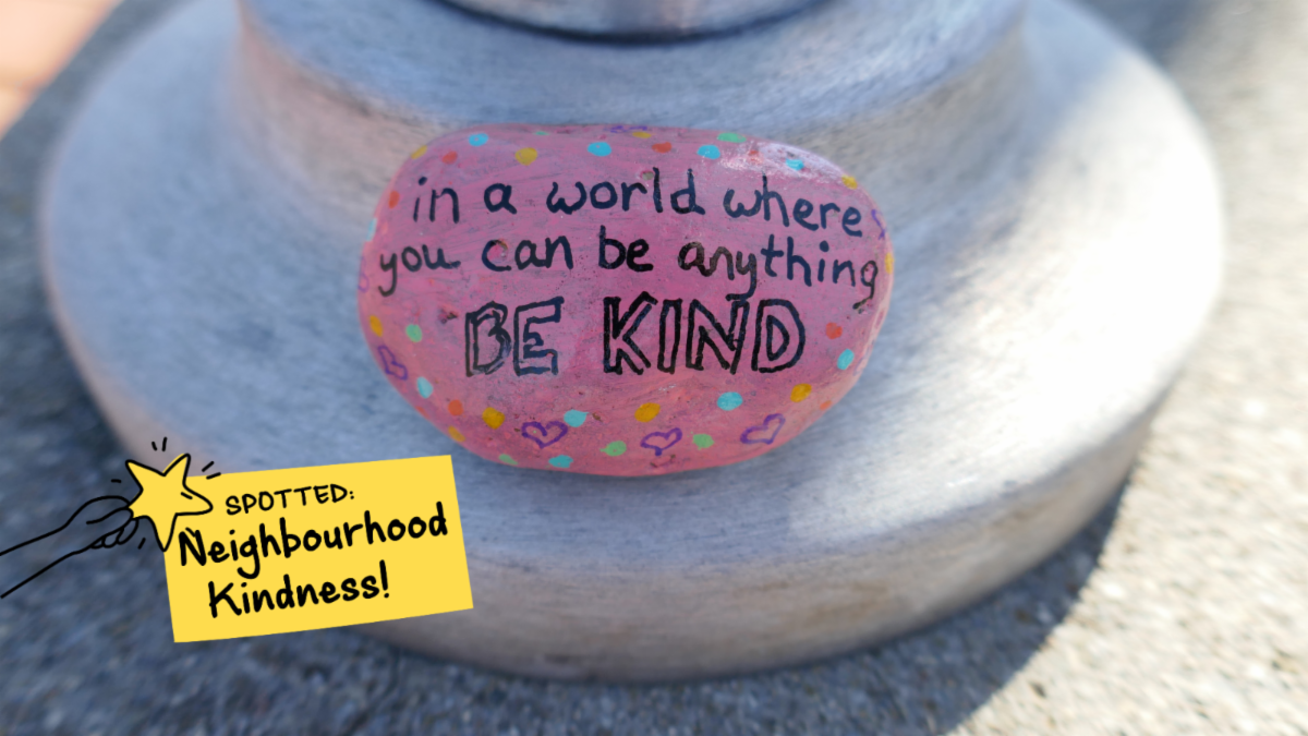 Painted rock that reads, in a world where you can be anything, be kind. Graphic ontop says spotted, neighbourhood kindness 