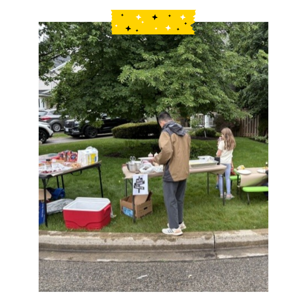 A few people standing on grass outside with tables full of food.