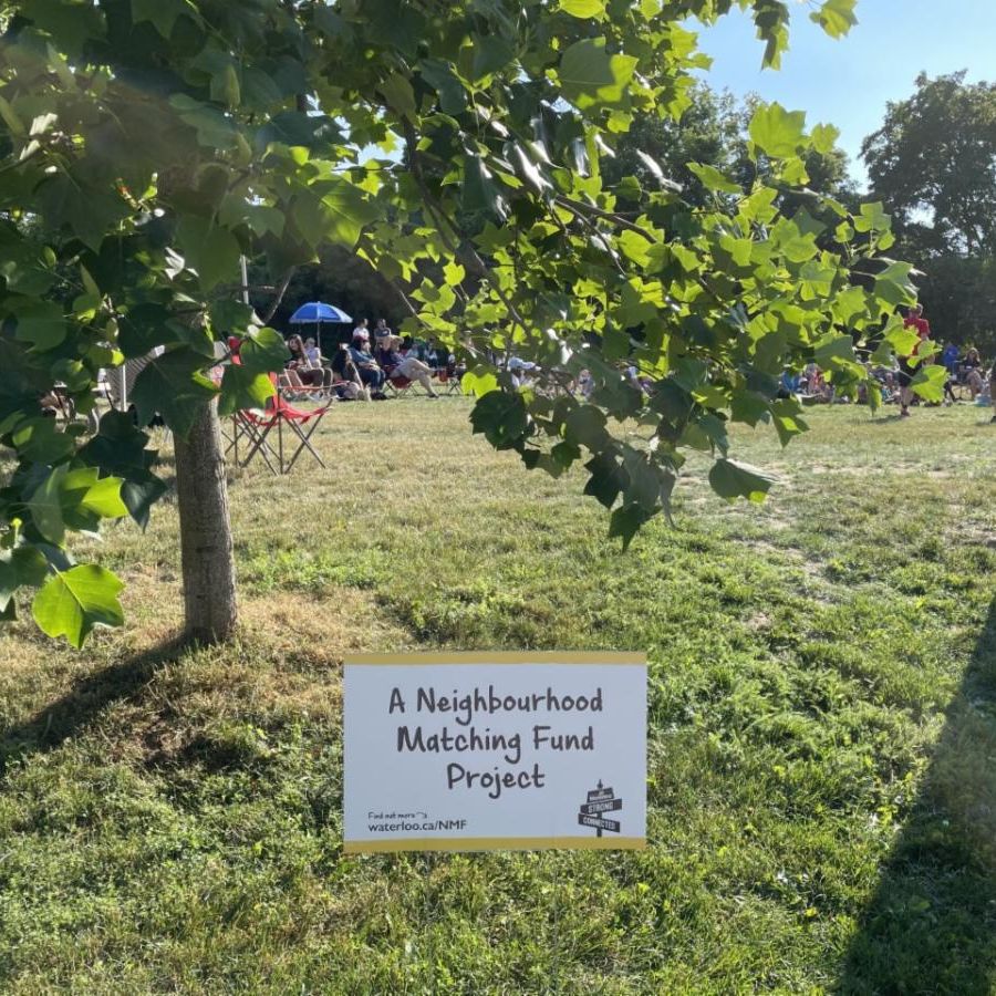 A park on a sunny day with tress and grass, with a Neighbourhood Matching Fund sign 