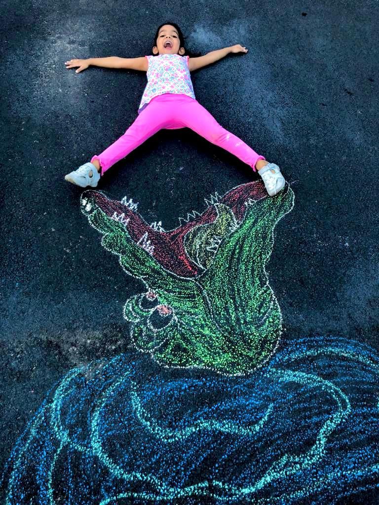 Chalk art of alligator, with a child laying on top as if being eaten by the alligator