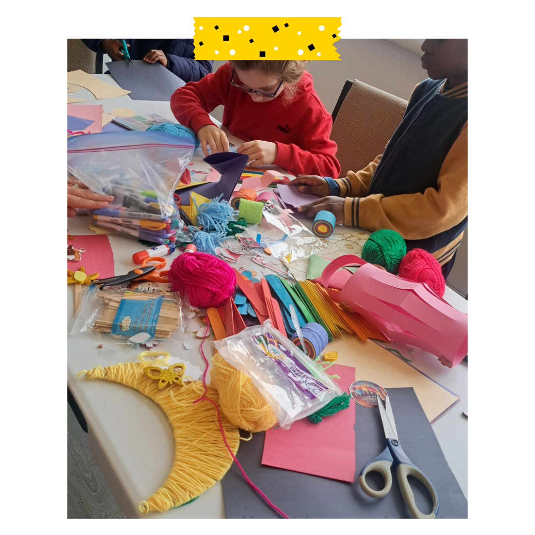 Two people at a table doing a craft lots of colourful paper and fun craft supplies on the table.