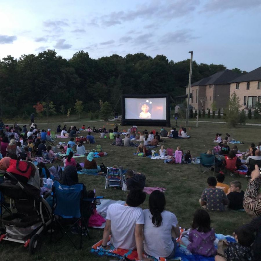 Group of people sitting outside watching a movie on a large projection screen