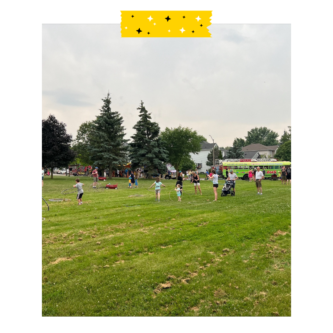 Lots of people standing with different activities outside on grass in a park lots of games going on.