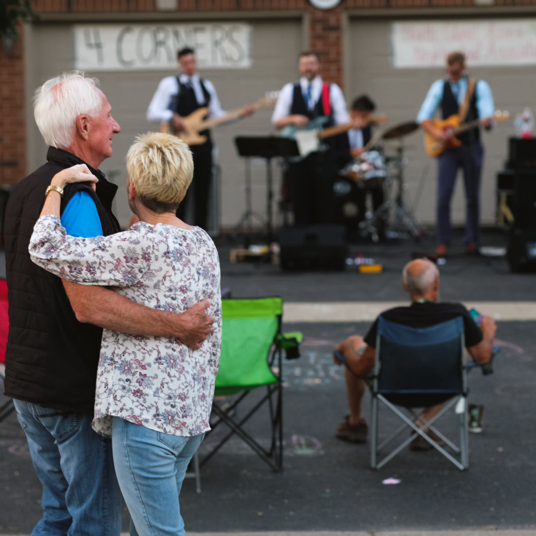 Couple with arms wrapped around each other watching a band play in front of a garage. 