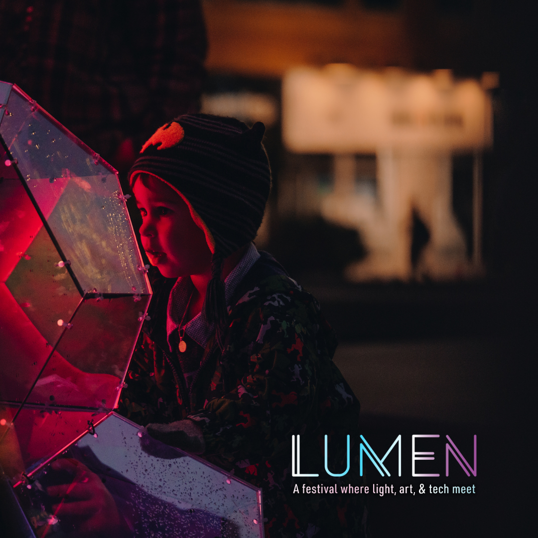 Child interacting with an art installation, in the shape of a glowing geometric globe. Text reads Lumen, a festival of light, art and tech. 