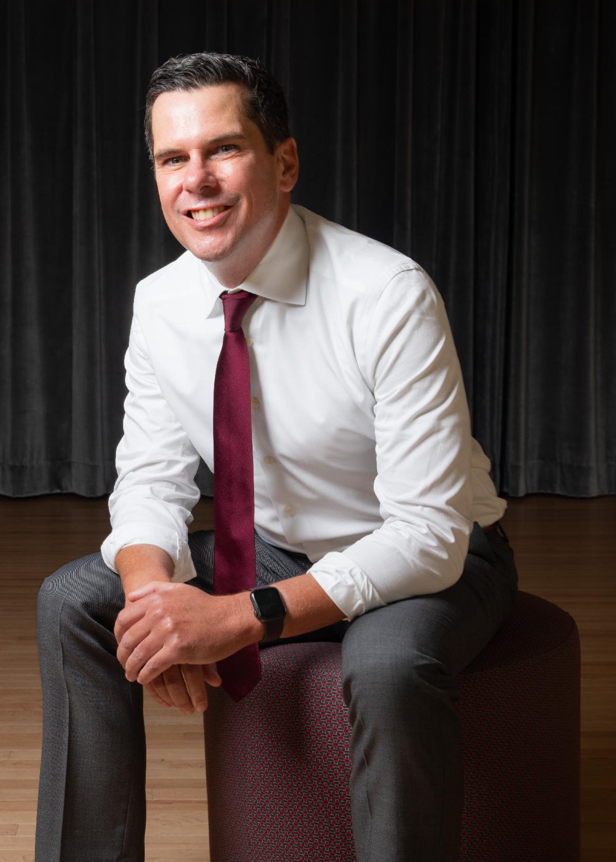 Dean Gudelunas sitting on a pink circle furniture piece on the first floor of the Ferman Center for the Arts