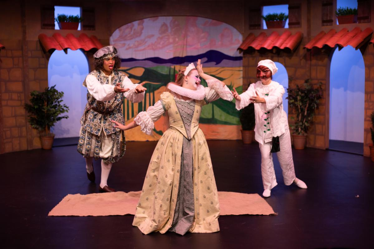 Main character in a dress holding her head. two other character behind her