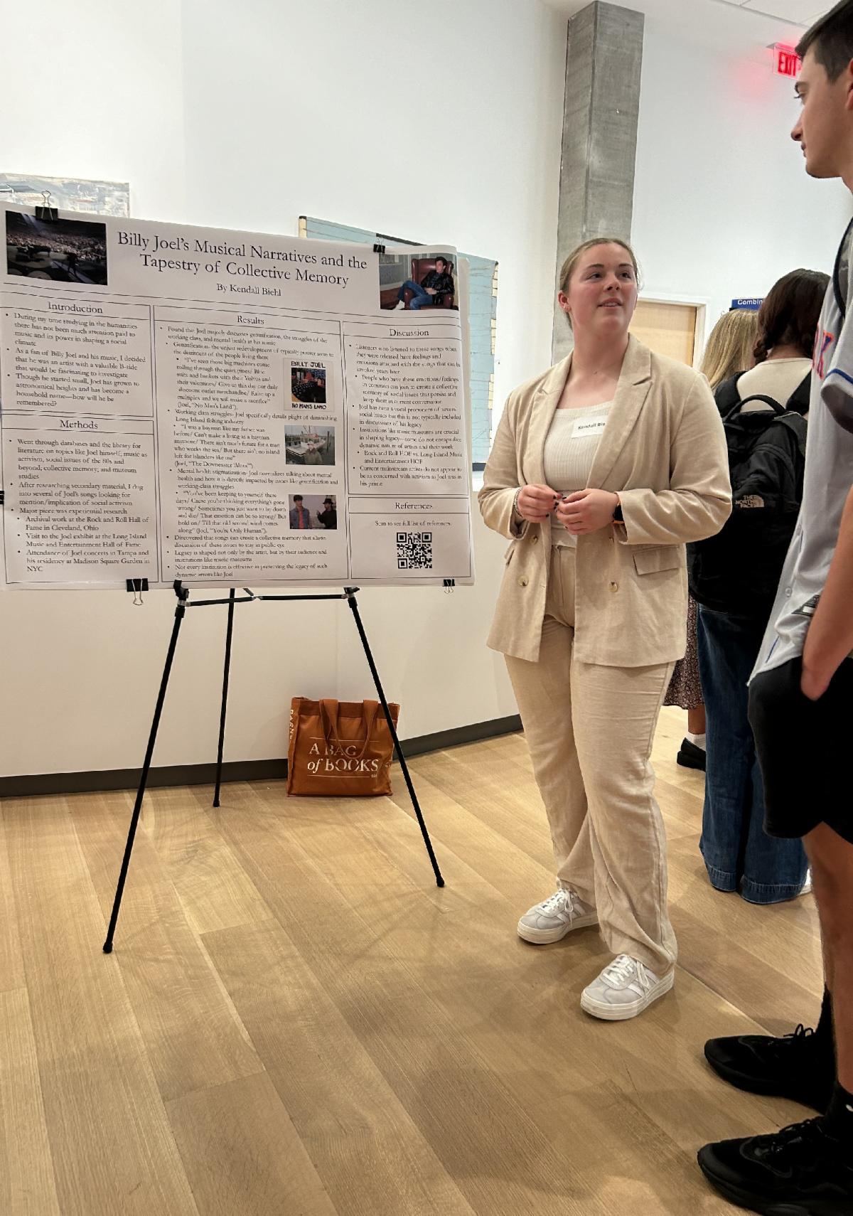 Kendall Biehl standing in front of a research poster and talking to a guest