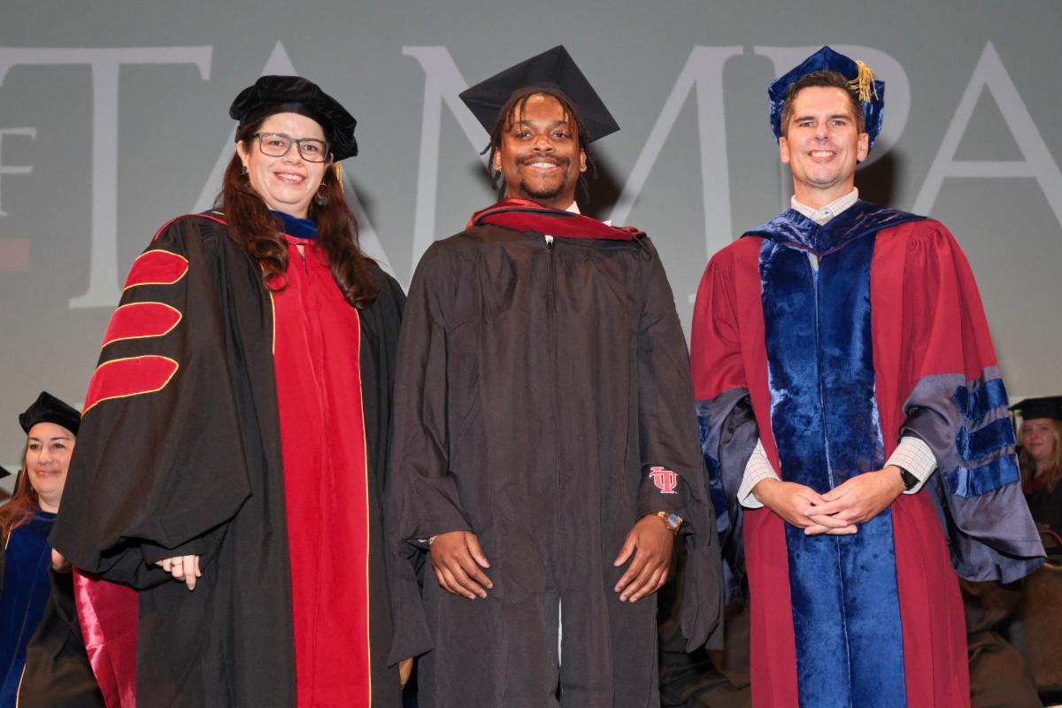 Dr. Gomez Vasquez and the dean academic regalia with a graduating senior in the middle
