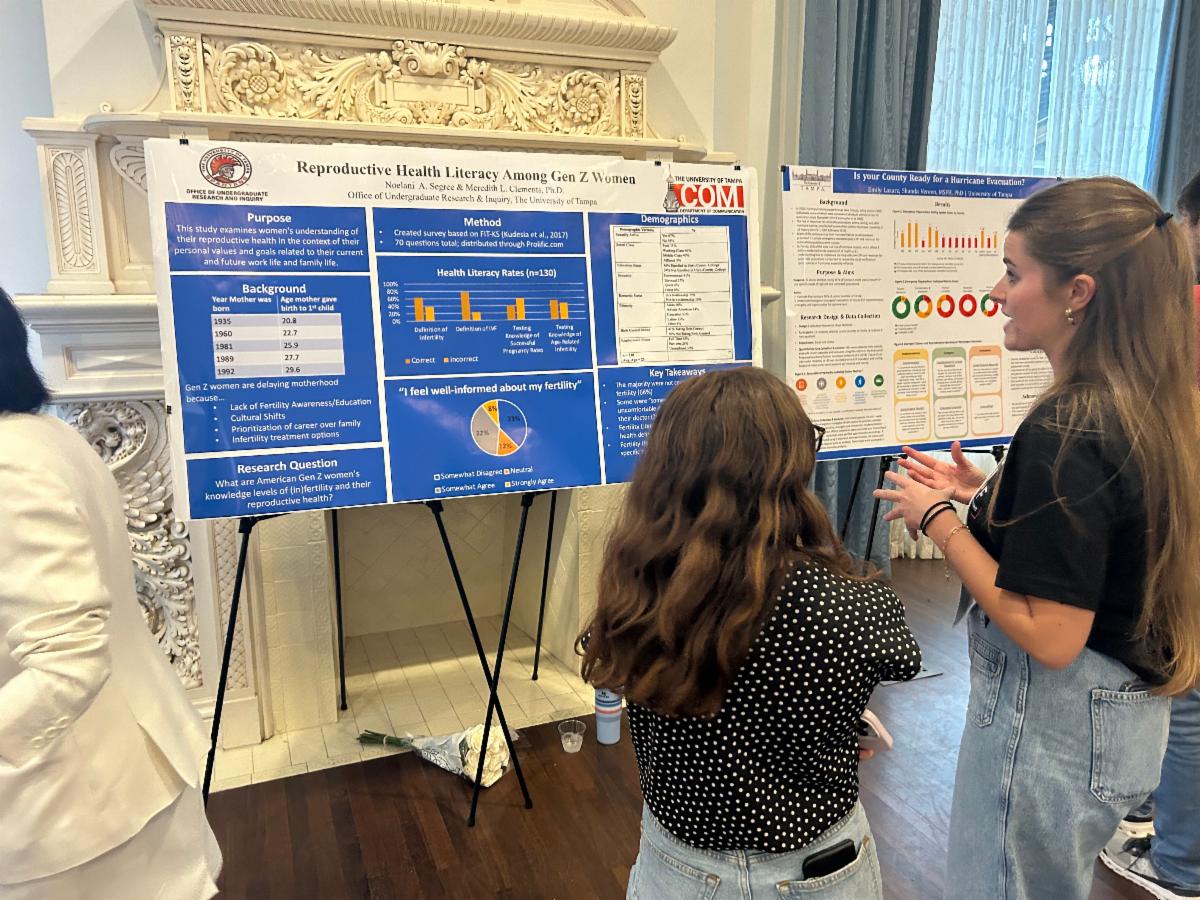 Noelani Segree standing in front of a research poster and talking to guests about it