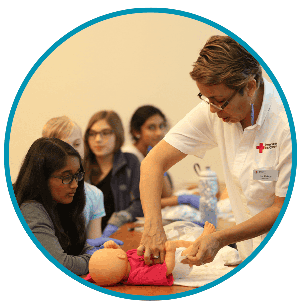 Three young girls around a Red Cross Instructor demonstrating proper diaper changing procedures.