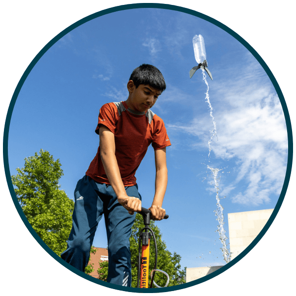 Young Boy pushing down a pump lever to rocket a bottle of water into the air as an experiment.