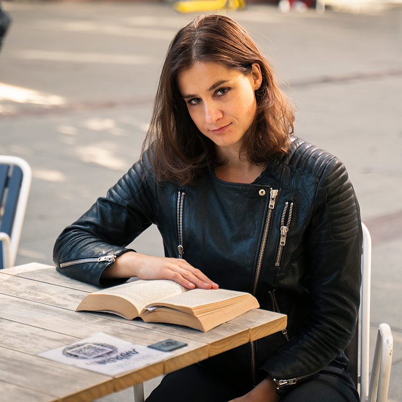 Portrett av Maria Kjos Fonn som sitter ved et kafébord med en bok.