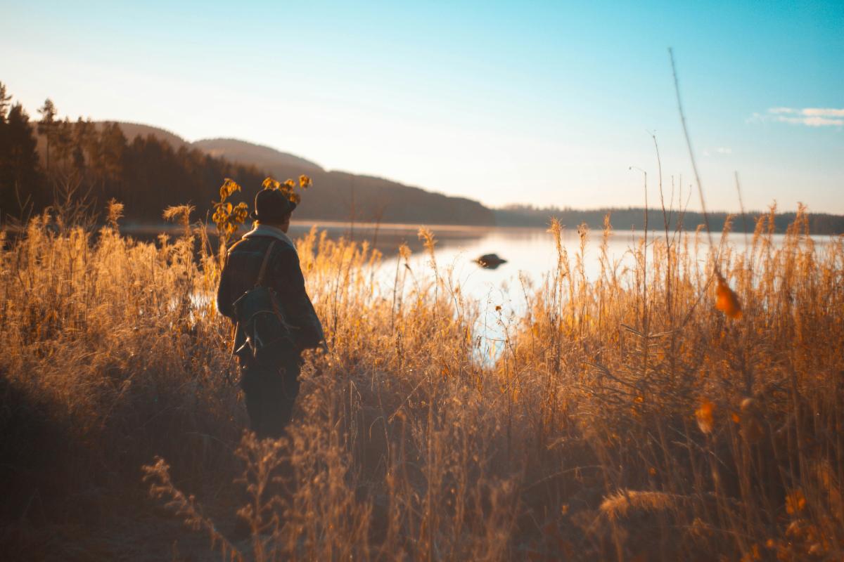 person standing on grass field near lake and mountain range. Photo by Thomas Bjornstad on Unsplash
