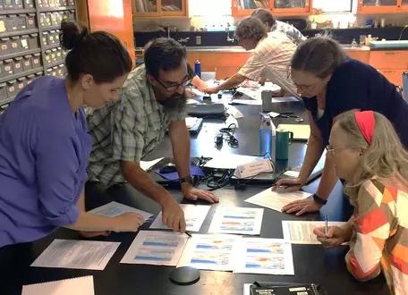 Adult learners standing around a table examining visual data sets
