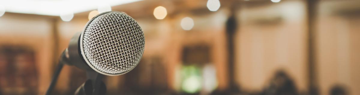Microphone in the foreground with a blurred out audience in the background | Adobe Stock
