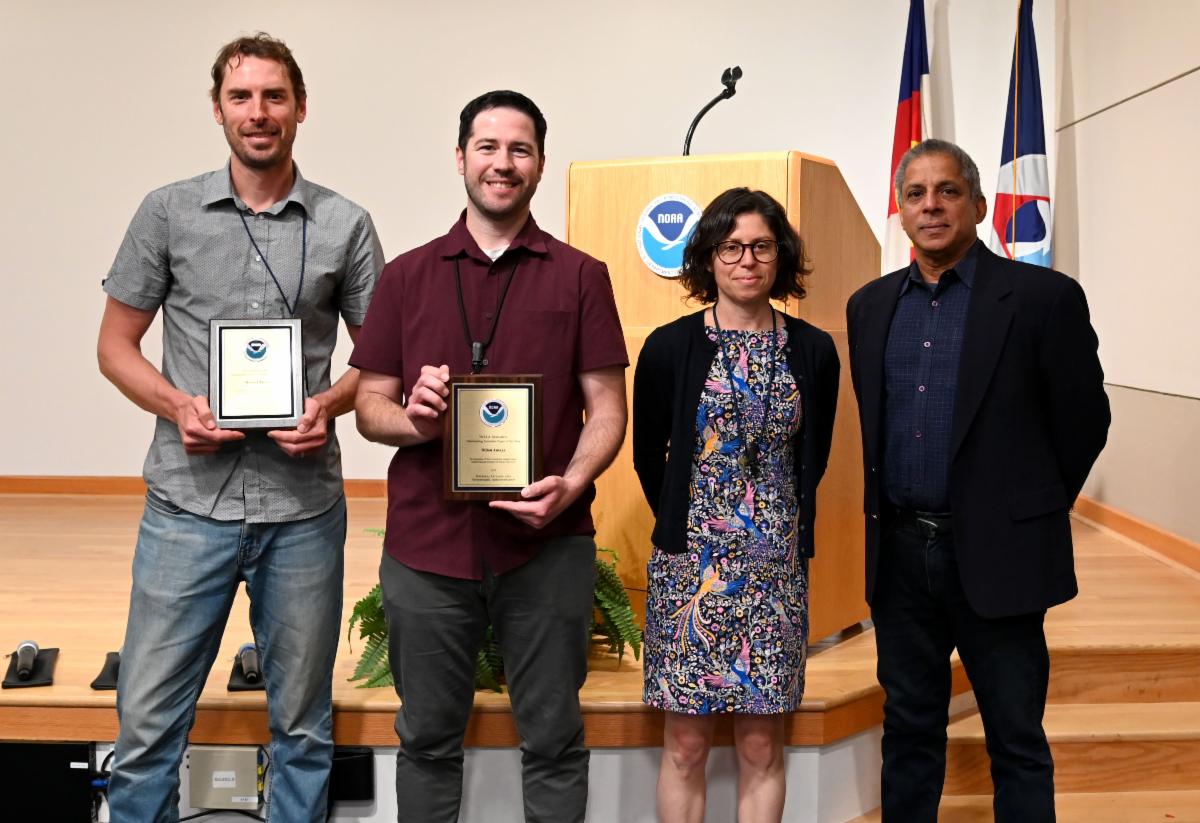 Four people stand in front of a NOAA podium with two holding awards