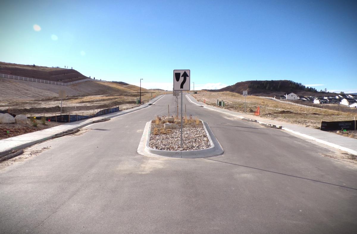 Divided road into Crystal Valley Ranch Filing 13 development under construction with graded hills on either side of road