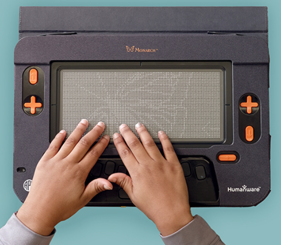 A monarch device with two hands reading the display. The device is black with orange buttons and the outline of a butterfly on the screen.