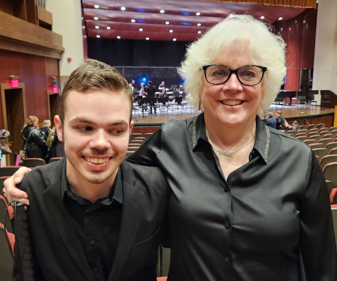 Leslie and Jacob standing in a concert hall. Both are wearing concert black and smiling facing the camera.