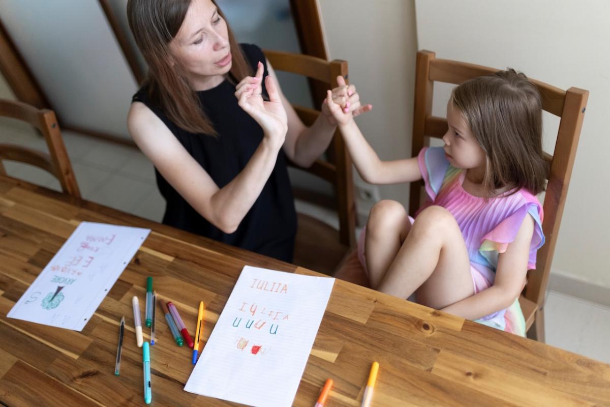 An intervener works on tactile sign language with a young student sitting at a table with paper and colored markers.