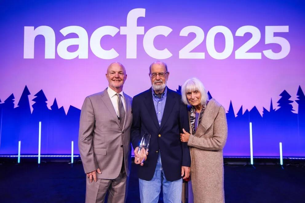Jeff Wine poses with his wife Marlene Wine, and Chris Penald in front of NACFC 2025 sign