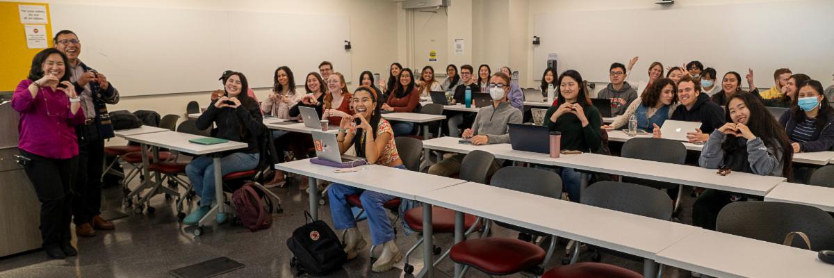 Professors Janine Bruce and Jorge DeLuna smile and pose with their students, making heart hands