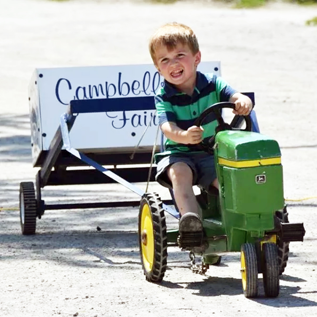 Child riding a pedal tractor towing a Campbellford Fair wagon.