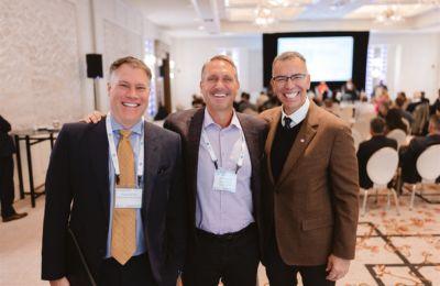 Three attendees together at Boston CEO, a session room behind them