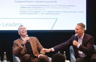 Two panelists laughing, one hand on the other's knee