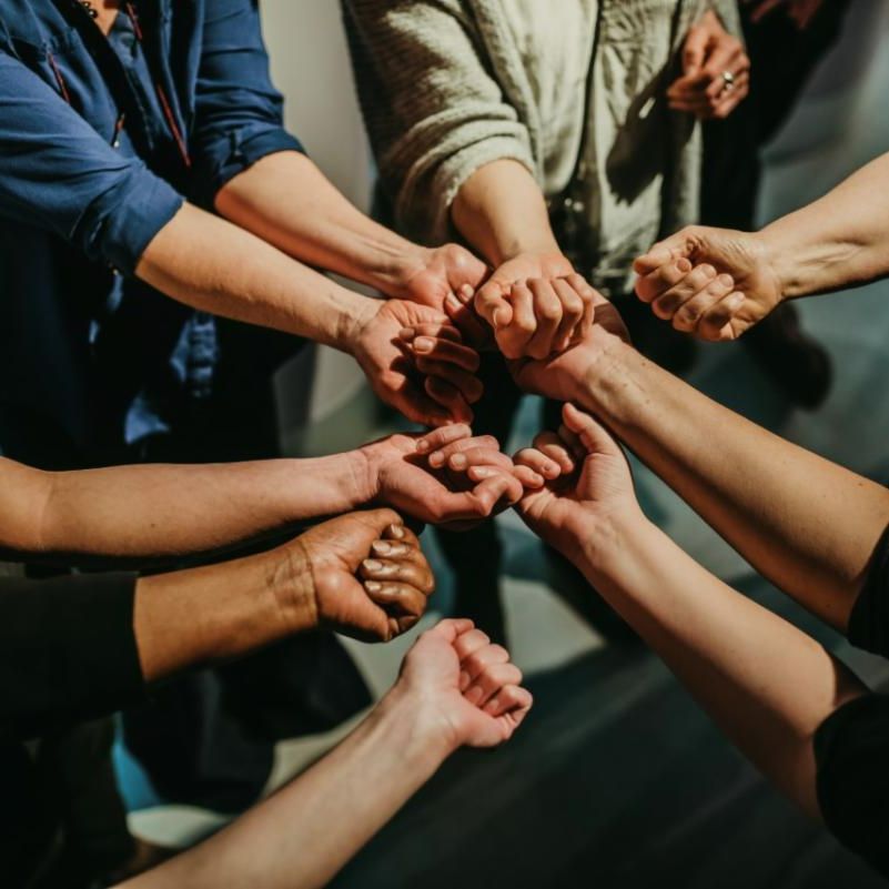 A photo of people with different skin colours putting their hands together in a circle.