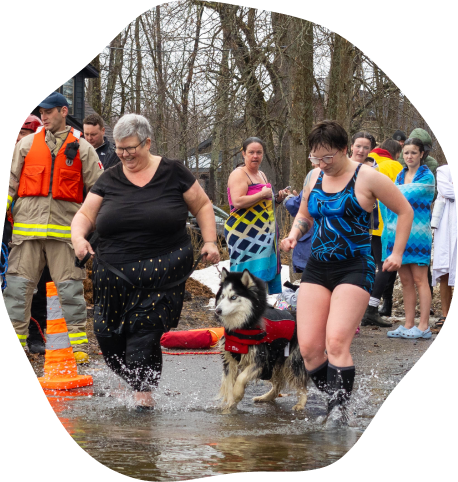 two women and a husky walking into a river with a crowd behind them