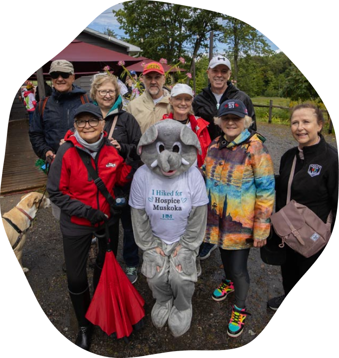 A group of people standing together with an elephant wearing a I Hiked For Hospice Muskoka tshirt