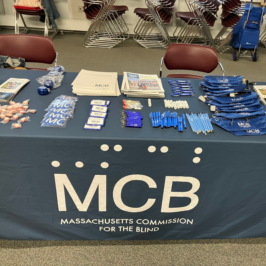 A table covered with an MCB-branded tablecloth, displaying brochures and promotional items