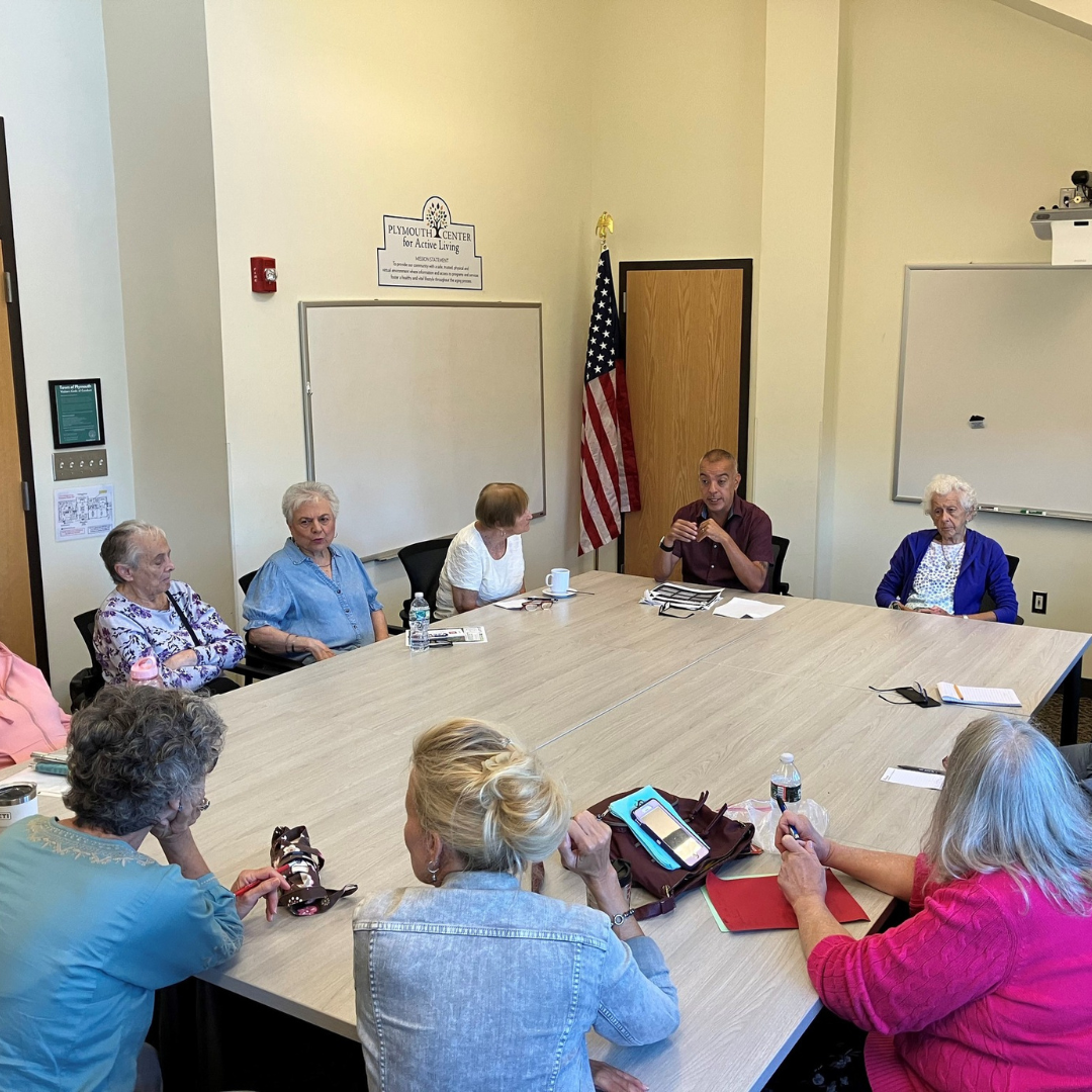 A group of people seated around tables, listening attentively as Chris Mittell presents