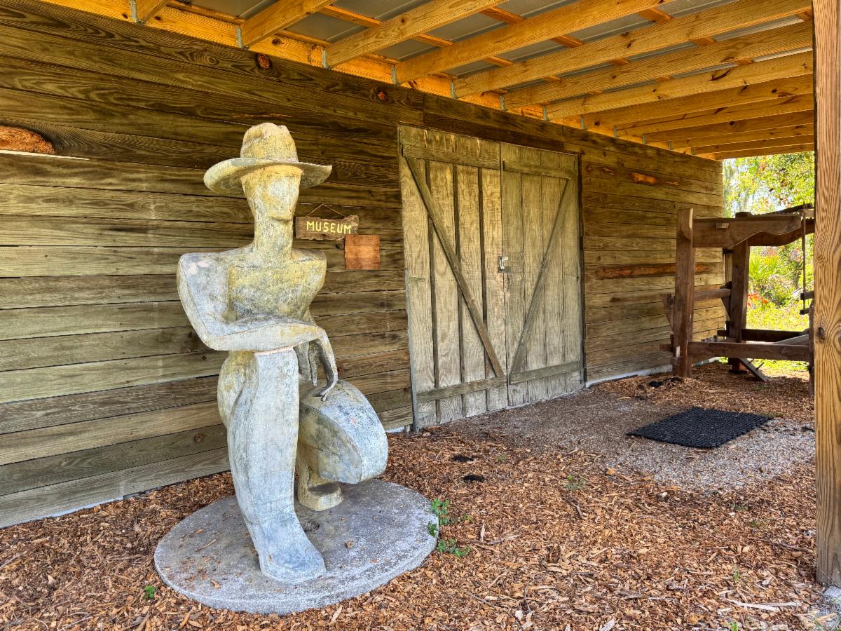 Historic building and statue photographed at the Crowley Museum and Nature Center. The statue depicts a farmer.