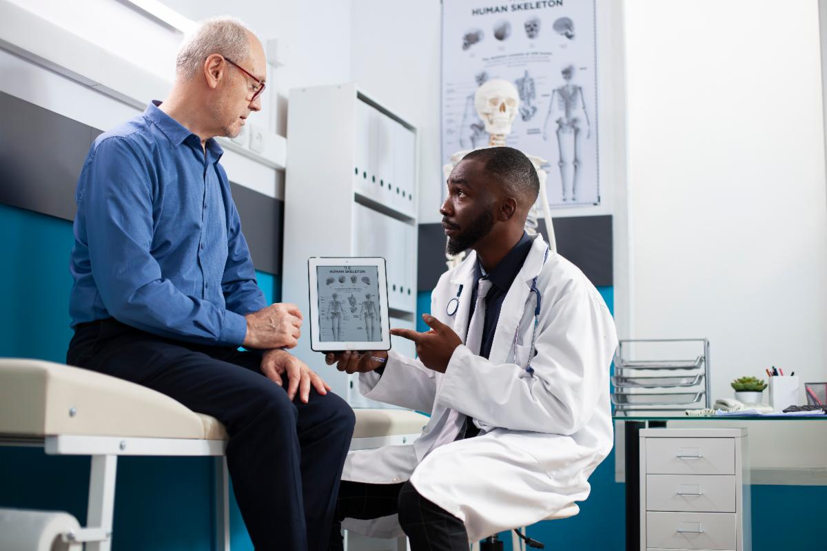 Clinician shows medical images on a tablet to a seated patient in an exam room.